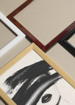 Widok z góry na cztery drewniane ramki od Plakatello® (w kolorze białym, czarnym, naturalnym kolorze drewna oraz lakierowaną elegancką brązową ramkę), w jednej z nich oprawiony jest plakat