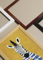 Widok z góry na cztery drewniane ramki, w jednej z nich oprawiony plakat zebra w swetrze z kawą na żółtym tle do pokoju dziecięcego