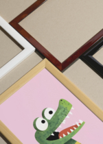 Widok z góry na cztery drewniane ramki, w jednej z nich oprawiony plakat zielony aligator na różowym tle do pokoju dziecięcego