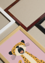 Widok z góry na cztery drewniane ramki, w jednej z nich oprawiony plakat gepard na różowym tle do pokoju dziecięcego