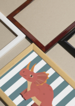 Widok z góry na cztery drewniane ramki, w jednej z nich oprawiony plakat dinozaur triceratops do pokoju dziecięcego koralowy skandynawski