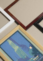 Widok z góry na cztery drewniane ramki, w jednej z nich oprawiony plakat Woolworth Building nocą Nowy Jork art deco vintage