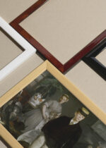 Widok z góry na cztery drewniane ramki, w jednej z nich oprawiony plakat Luncheon w pracowni Édouard Manet 1868 reprint