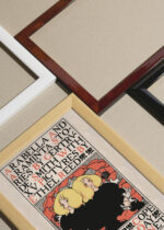 Widok z góry na cztery drewniane ramki, w jednej z nich oprawiony plakat Ethel Reed Arabella and Araminta vintage 1895