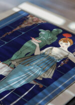 Widok z góry na cztery drewniane ramki, w jednej z nich oprawiony plakat Art Déco Perłowa Fontanna George Barbier 1914