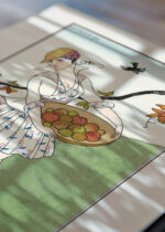 Widok z góry na cztery drewniane ramki, w jednej z nich oprawiony plakat Art Deco George Barbier kobieta w ogrodzie 1914