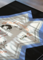 Widok z góry na cztery drewniane ramki, w jednej z nich oprawiony plakat Art Deco George Barbier Falbalas et fanfreluches