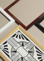 Widok z góry na cztery drewniane ramki, w jednej z nich oprawiony plakat geometryczny czarno-biały krzyż z promieniami S.J. de Mesquita