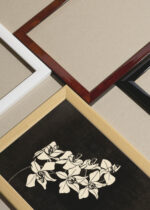 Widok z góry na cztery drewniane ramki, w jednej z nich oprawiony plakat czarno-biały Orchidea 1916 Samuel Jessurun de Mesquita