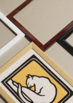 Widok z góry na cztery drewniane ramki, w jednej z nich oprawiony plakat Kot liżący łapę Julie de Graag minimalistyczny