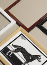 Widok z góry na cztery drewniane ramki, w jednej z nich oprawiony plakat pies czarno-biały drzeworyt Julie de Graag 1917