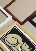 Widok z góry na cztery drewniane ramki, w jednej z nich oprawiony plakat czarno-biały śpiący kot 1918 Julie de Graag