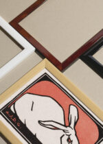 Widok z góry na cztery drewniane ramki, w jednej z nich oprawiony plakat królik Julie de Graag 1916 czerwone tło vintage