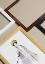 Widok z góry na cztery drewniane ramki, w jednej z nich oprawiony plakat Cappiello kobieta w złotym kapeluszu z różami