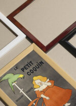 Widok z góry na cztery drewniane ramki, w jednej z nich oprawiony plakat Dziewczynka z papugą Leonetto Cappiello vintage