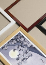 Widok z góry na cztery drewniane ramki, w jednej z nich oprawiony plakat Kwitnąca wiśnia w świetle księżyca Ohara Koson błękitno-szary