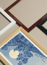 Widok z góry na cztery drewniane ramki, w jednej z nich oprawiony plakat Kwitnąca wiśnia w świetle księżyca Ohara Koson ciemny błękit