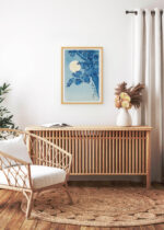 Aranżacja wnętrza, na ścianie wisi plakat w ramce: Kwitnąca wiśnia w świetle księżyca Ohara Koson ciemny błękit