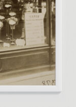 Zbliżenie na detale plakatu oprawionego w drewnianą białą ramkę od Plakatello®: E. Atget witryna salonu fryzjerskiego Paryż 1912