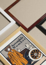 Widok z góry na cztery drewniane ramki, w jednej z nich oprawiony plakat Automobile number kobieta przy samochodzie (1903)