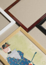 Widok z góry na cztery drewniane ramki, w jednej z nich oprawiony plakat Kobieta trzymająca czerwoną parasolkę (1896)