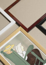 Widok z góry na cztery drewniane ramki, w jednej z nich oprawiony plakat Kobieta czytająca książkę w fotelu bujanym (1899)