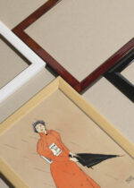 Widok z góry na cztery drewniane ramki, w jednej z nich oprawiony plakat Kobieta trzymająca czarny parasol (1894)