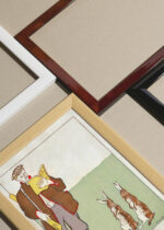 Widok z góry na cztery drewniane ramki, w jednej z nich oprawiony plakat Mężczyzna czytający książkę z zającami (1895)