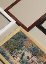 Widok z góry na cztery drewniane ramki, w jednej z nich oprawiony plakat Renoir W Bretanii 1886 En Bretagne kobiety w ogrodzie