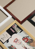 Widok z góry na cztery drewniane ramki, w jednej z nich oprawiony plakat japoński aktor kabuki w białej peruce Toyohara Kunichika