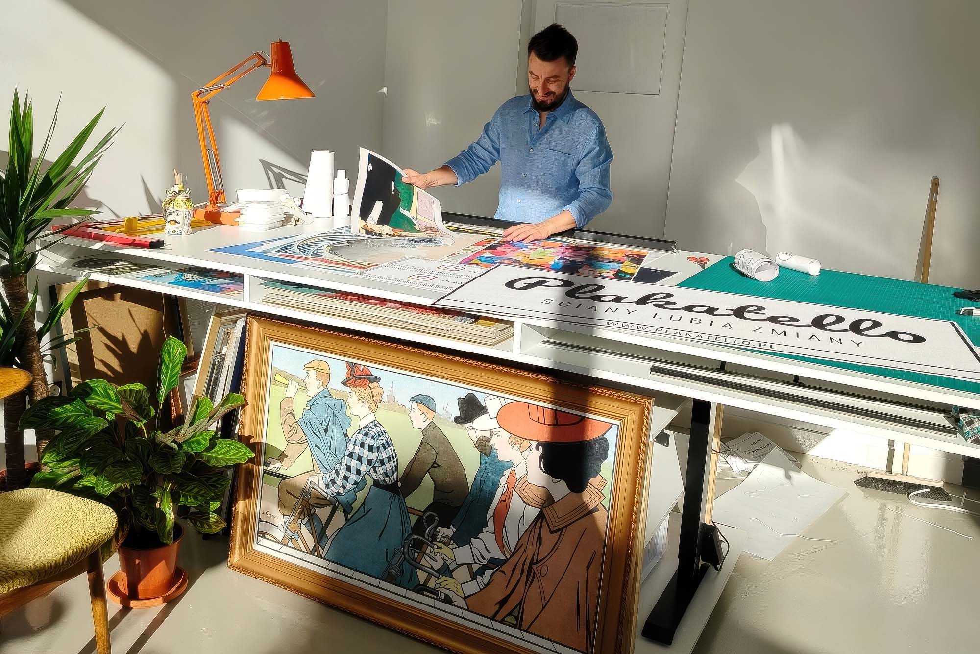 Plakat na płótnie w ramie JOB Alfons Mucha 55x75 cm 1 Fotografia z sesji zdjęciowej w pracowni Plakatello® w Lublinie. Właściciel w sytuacji roboczej, trzymający wydruki plakatów. Polska marka plakatów dekoracyjnych, gdzie wszystkie produkty powstają z dbałością o najmniejszy szczegół. Od druku po oprawę – każdy plakat przechodzi przez ręce zespołu, gwarantując najwyższą jakość.